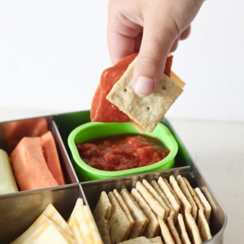 DIY Pizza Lunchables 7 | Milk & Honey Nutrition Hand dipping pepperoni, cheese, and a cracker into pizza sauce from a DIY pizza Lunchable.