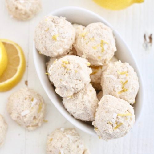 no bake lemon cheesecake bites 6 | Milk & Honey Nutrition Overhead view of no-bake lemon protein bites in a white bowl with fresh lemon and coconut.