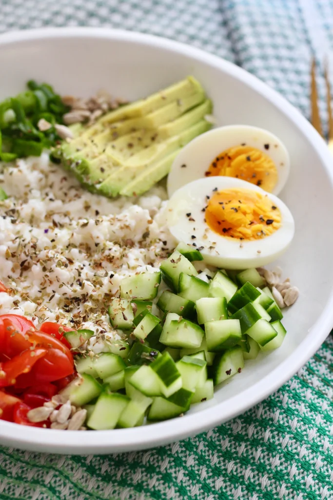 savory cottage cheese breakfast bowl 4 | Milk & Honey Nutrition Healthy savory cottage cheese breakfast bowl with avocado, hard-boiled egg halves, cucumber, tomatoes, greens, seeds, pistachios, on a cottage cheese base. Food pairing for blood sugar examples